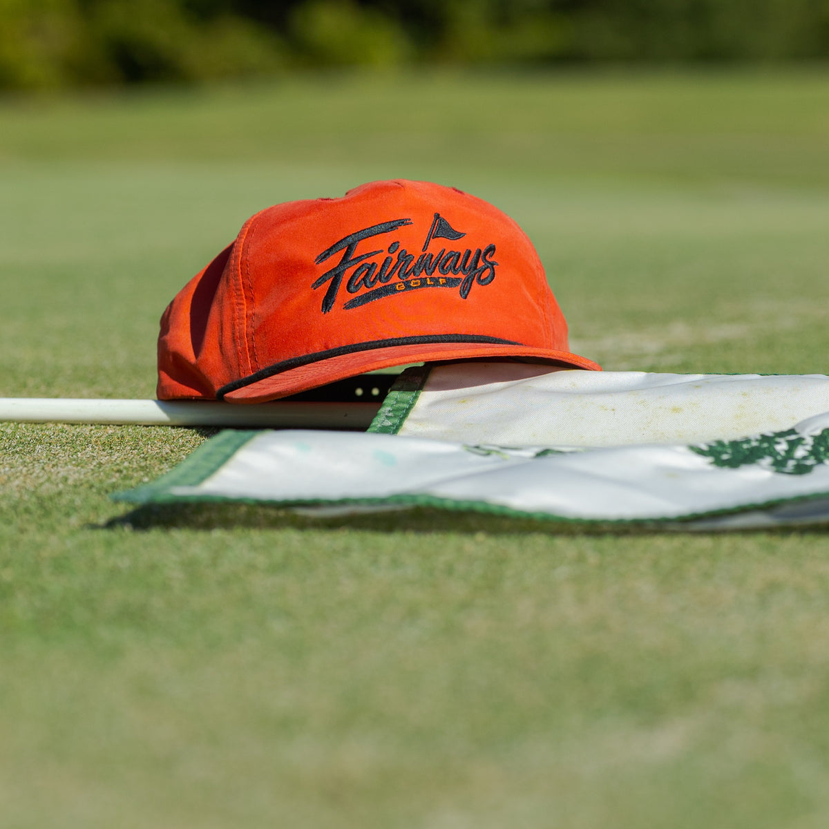 Orange Fairways rope cap resting by a flagstick on the putting green